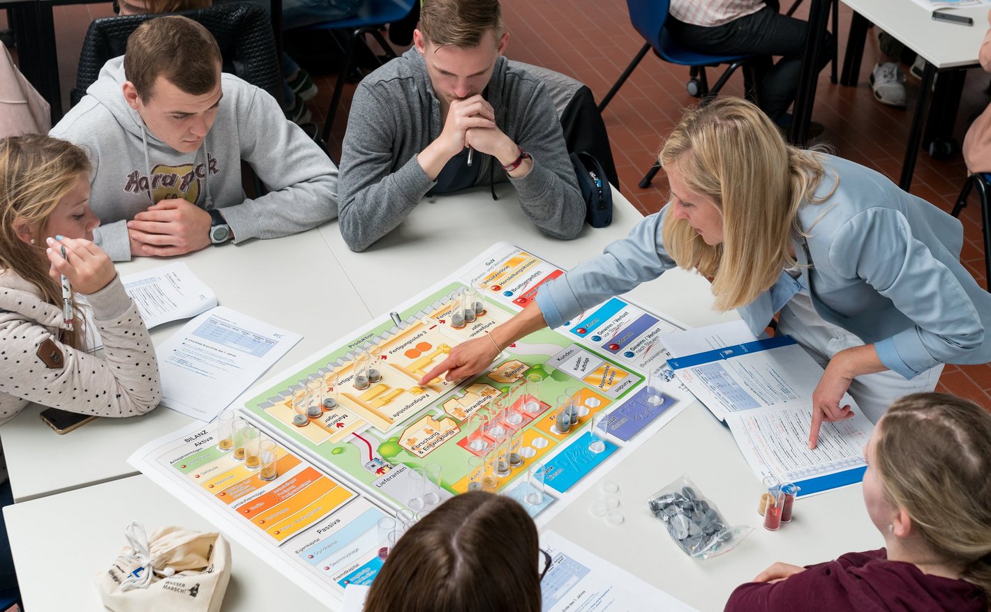 Students sit at a table with their mentor and carry out a business game
